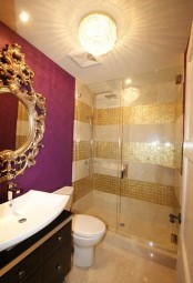 a glam bathroom with neutral and gold tiles in stripes, a purple accent wall, a refined mirror in a gilded frame and a black vanity