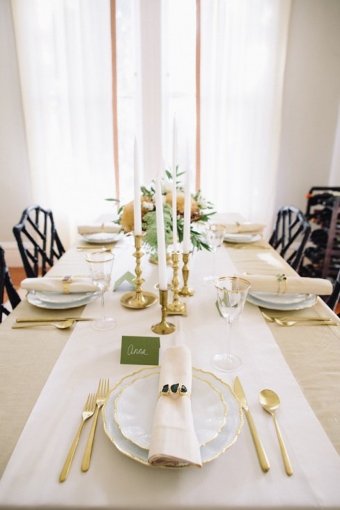 A neutral and refined Thanksgiving tablescape with neutral linens, greenery, warm colored blooms, candles and gold cutlery for a chic touch
