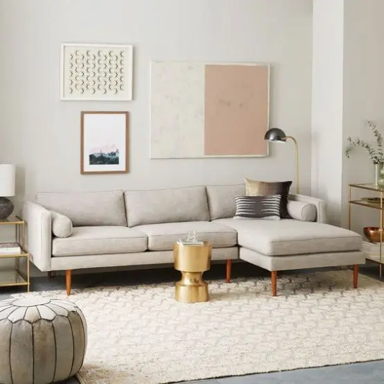 a neutral mid-century modern living room with a grey sectional, a neutral rug, a grey pouf, a gold side table and a lovely gallery wall