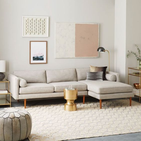 A neutral mid century modern living room with a grey sectional, a neutral rug, a grey pouf, a gold side table and a lovely gallery wall