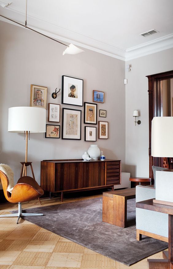 A mid century modern living room done in neutrals, with stained furniture, a leather chair, a credenza, a gallery wall and table lamps