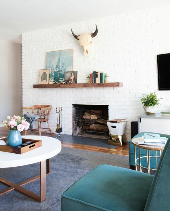 A stylish mid century modern living room with a white brick fireplace, teal chairs, a round coffee table, some beautiful decor and a skull