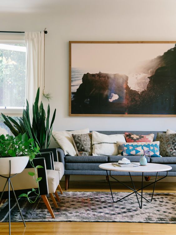 A pretty mid century modern living room with a grey sofa, bright pillows, a printed rug, potted greenery and a print is amazing