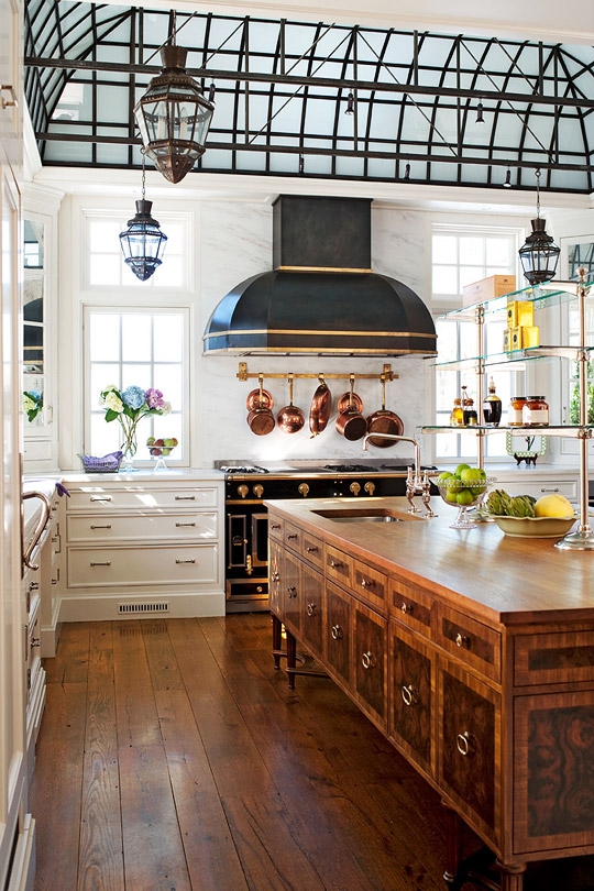 a beautiful vintage kitchen with white cabinetry, a large stained kitchen island, a refined black and copper cooker and a matching black and copper hood is amazing