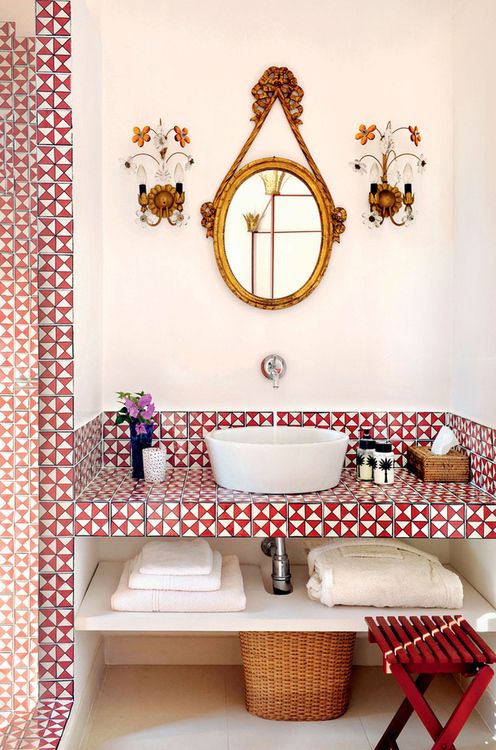 A refined geometric bathroom in red and white, with geo tiles, a built in vanity with storage, a chic mirror and refined wall sconces