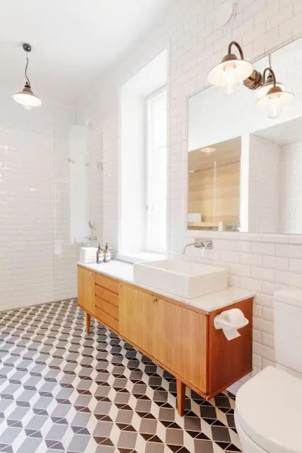 A mid century modern bathroom with geometric tiles on the floor, white subway tiles on the walls and a wooden vanity with white appliances
