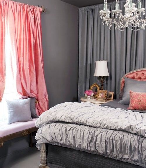 an elegant grey and coral pink bedroom with chic curtains, an upholstered bed, an elegant chandelier and lamp, an upholstered bench