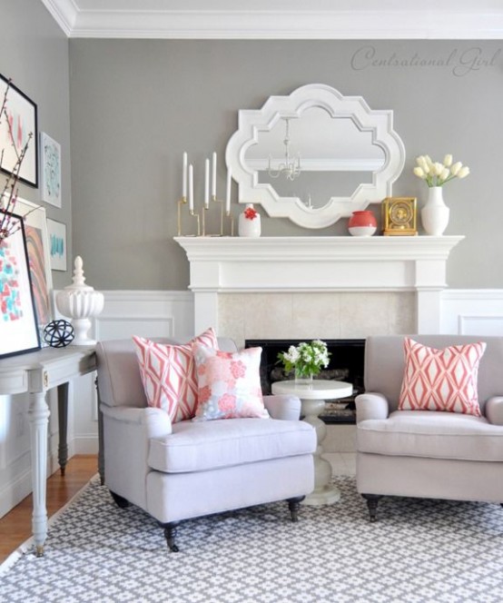 a farmhouse-inspired living room with grey walls, a coffee table, a white fireplace and lots of prints and subtle coral touches