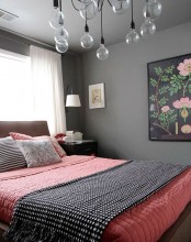 a catchy grey and coral bedroom with a bulb chandelier, a bright artwork, wall lamps and dark nightstands