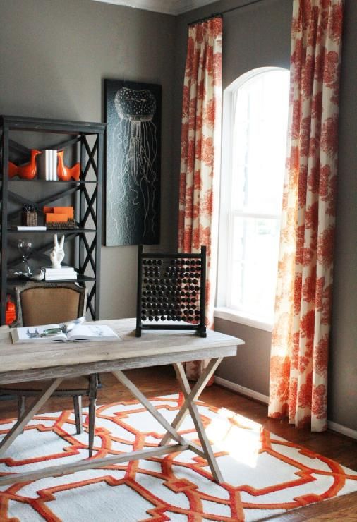 a stylish grey and coral home office with grey walls, a wooden desk, printed textiles, a black shelf and a dark artwork
