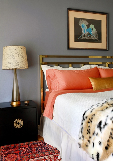 a grey and coral bedroom, a dark nightstand, bright bedding and an artwork and a lamp