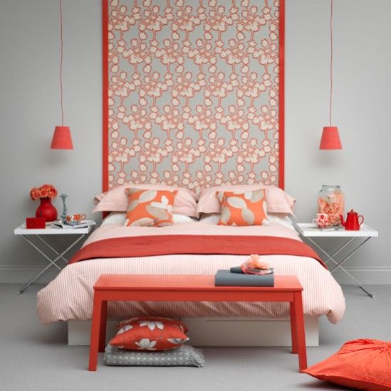 a contemporary grey and coral bedroom with a printed statement wall, grey walls, coral lamps, pillows and a bench and bright bedding