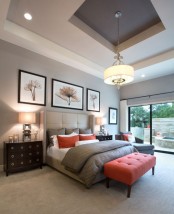 a modern bedroom done in light greys, with a coral bench and pillows, dark stained furniture and a glazed wall