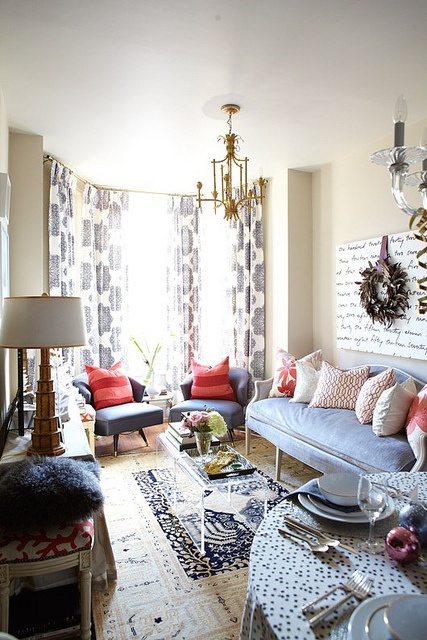 a quirky living room done in light greys, ivory and coral touches, catchy chandeliers, pritned pillows and vintage lamps