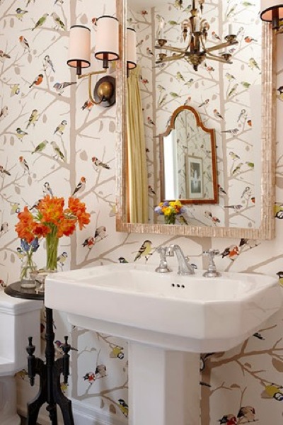 A cheerful guest toilet with a free standing sink, floral and bird print wallpaper, wall lamps and a framed mirror