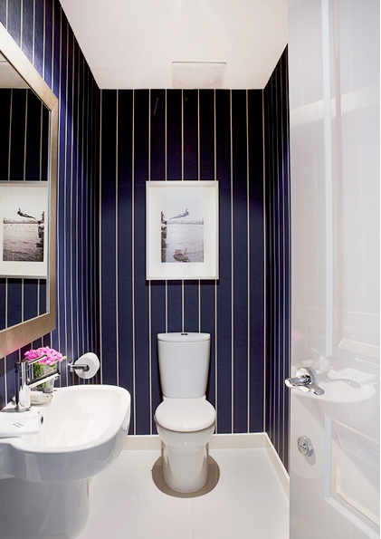A small guest toilet with navy and white thin stripe wallpaper, a white wall mounted sink and an artwork