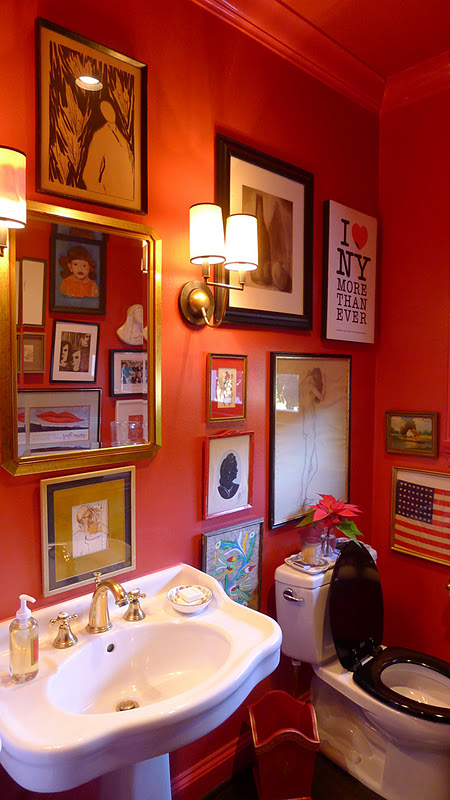 A bold guest toilet with bright orange walls, a free standing sink, a mirror and a whole gallery wall