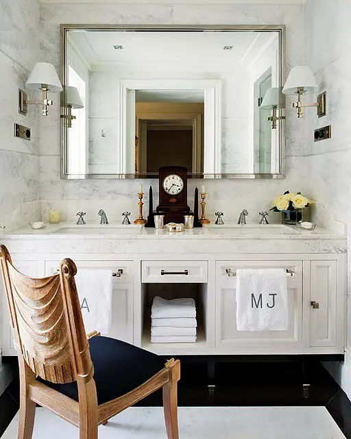 an elegant guest toilet with a large mirror, a neutral mirror with storage and a stone countertop plus a vintage and refined chair