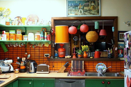 a bold kitchen with green cabinets, an orange tile backsplash, a wooden shelf and some orange touches is very fun and whimsy