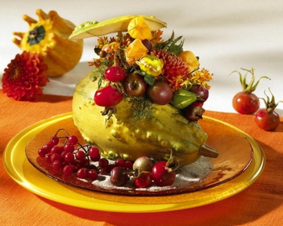 a gourd filled with bright blooms and vegetables and berries on the plate is a very bold and chic Thanksgiving decoration