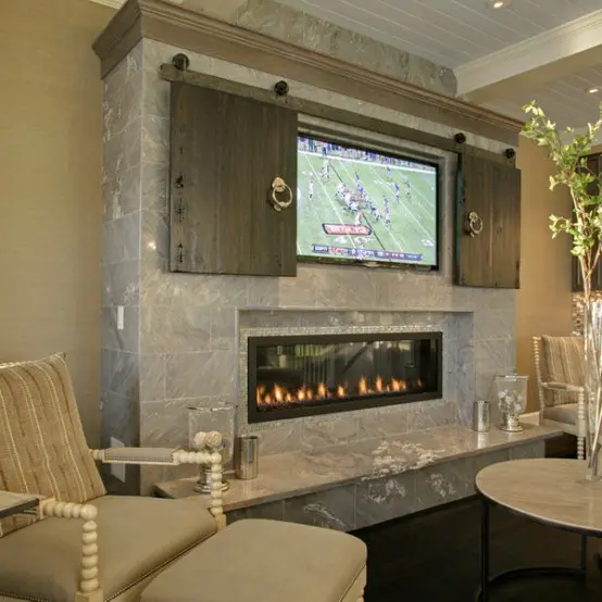 a fireplace clad with stone tile, a TV over the fireplace and wooden barn doors hiding the TV