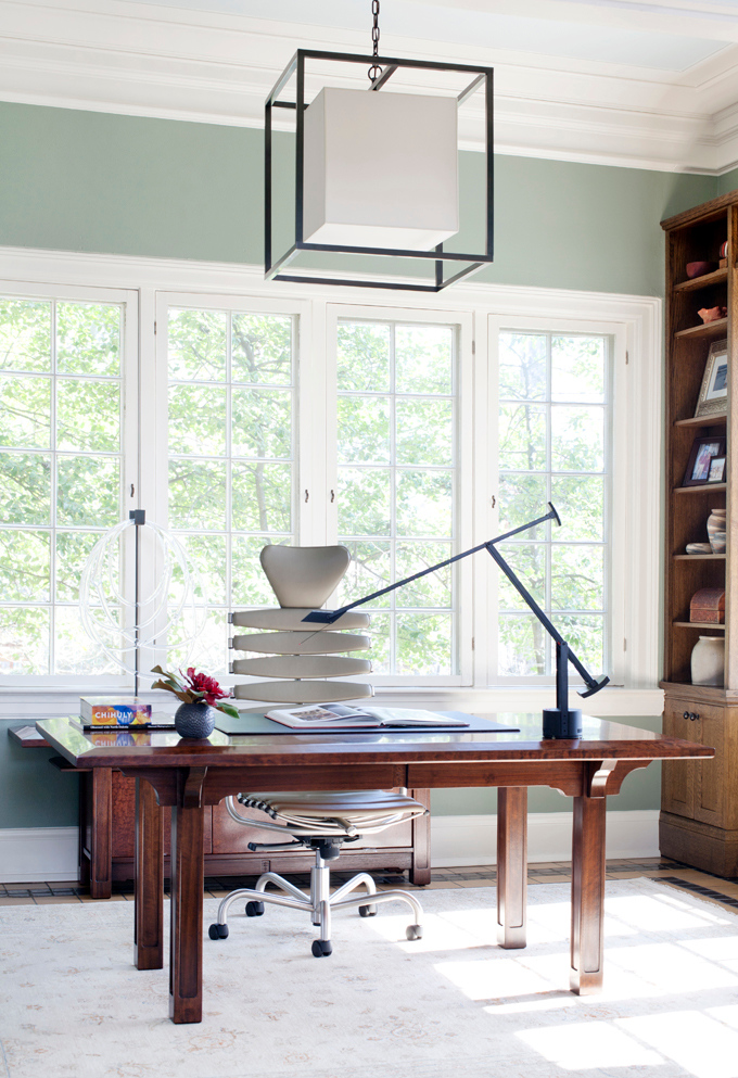 An eye catchy mid century modern home office with a stained desk, a neutral chair, a stained storage unit, a black lamp and a catchy pendant lamp