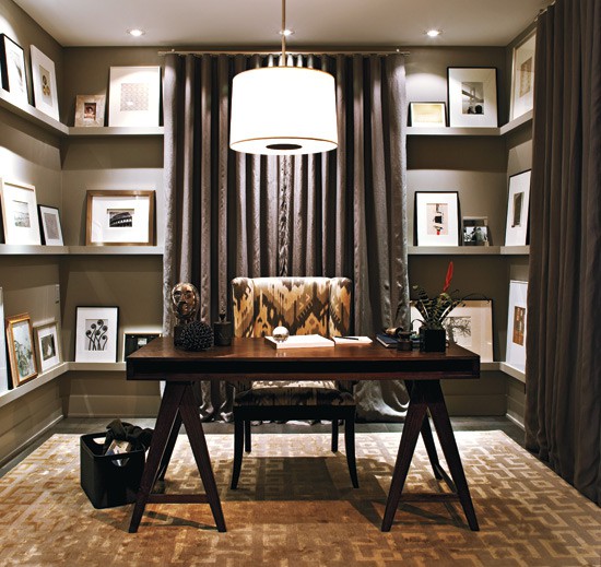 an elegant home office with grey walls and gallery walls on ledges, with a trestle desk, an ikat print chair, built-in lights and a pendant lamp