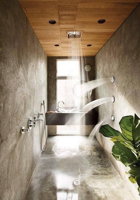 A contemporary home space done with concrete, with a wooden ceiling and some spa showers, a built in vanity by the window and a potted plant