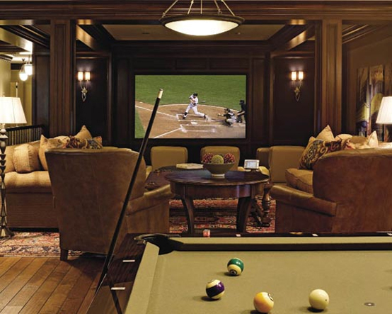 An elegant home theater room with a screen clad with dark stained wood, beige and tan seating furniture, a dark stained table and a pool table