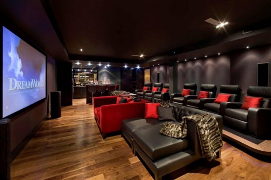 a dark-colored home theater with deep brown walls, a large screen, built-in lights, a red sofa and brown leather chairs around