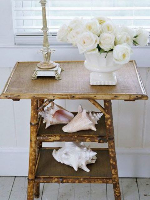 a rustic console table covered with burlap and with large shells and white blooms for beachy decor