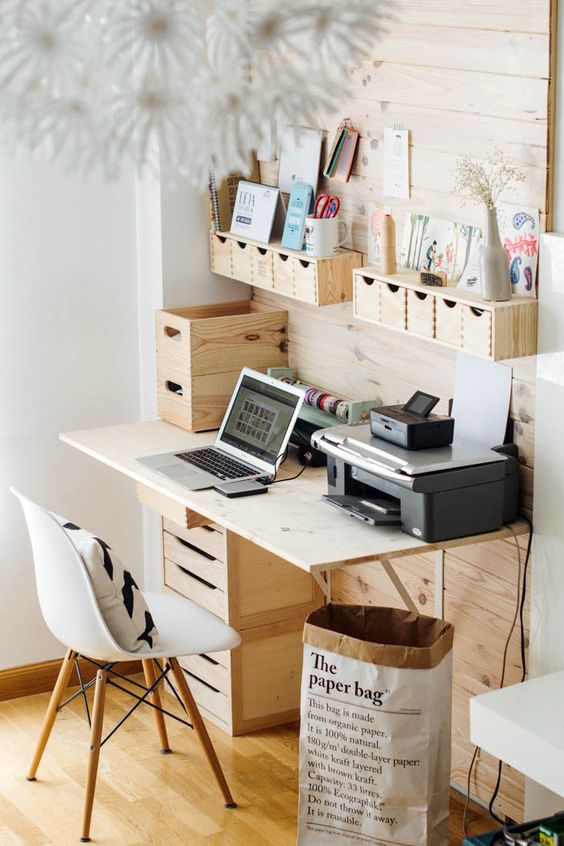A wooden wall mounted storage unit with some holders and little wooden drawers that hold pencils and pens
