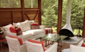 a modern outdoor sitting space wiht a white suspended Malm fireplace, white seating furniture, orange pillows and a glass coffee table