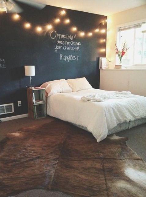a farmhouse bedroom with a chalkboard accent wall, a string light on this wall, a cozy bed with neutral bedding and a stained nightstand