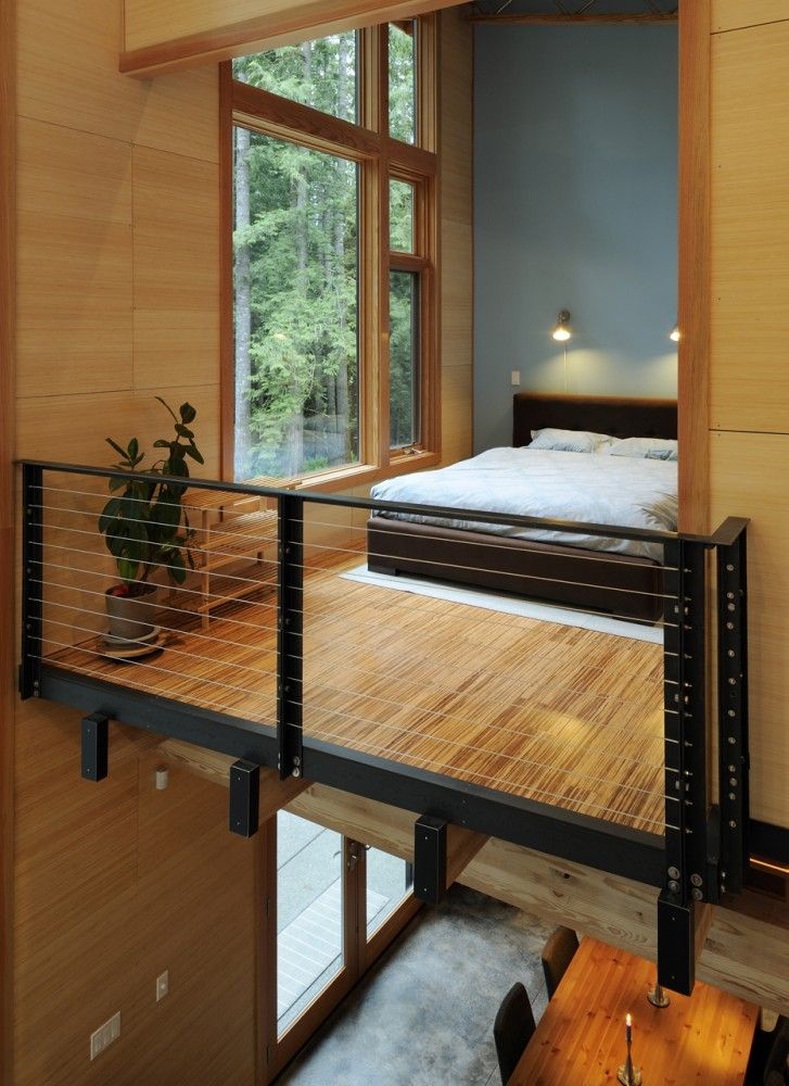 A Japandi loft bedroom with a large window, a bamboo floor, a dark stained bed with neutral bedding and some lights over the bed is cool and relaxing