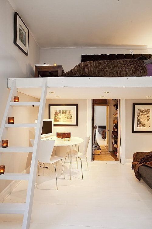 A small neutral space with a ladder up and a loft bedroom, a bed with dark bedidng and a low dark stained coffee table