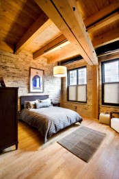 a welcoming modern bedroom with dark stained furniture, wooden beams and an exposed brick wall – both these features add interest to the space