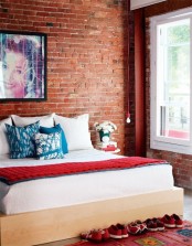 a bright contemporary bedroom with a comfy bed, a hanging bulbb and an exposed brick statement wall that takes over the whole space