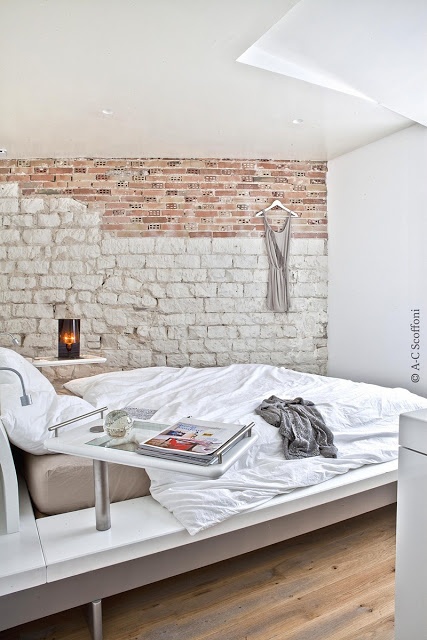 An ultra modern bedroom with a chic bed is made bolder and catchier with a faux stone and brick wall created with a mural