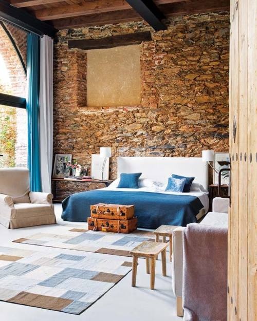 an eclectic bedroom with a stone wall, contemporary and vintage furniture and a glazed wall for more light and enjoying views
