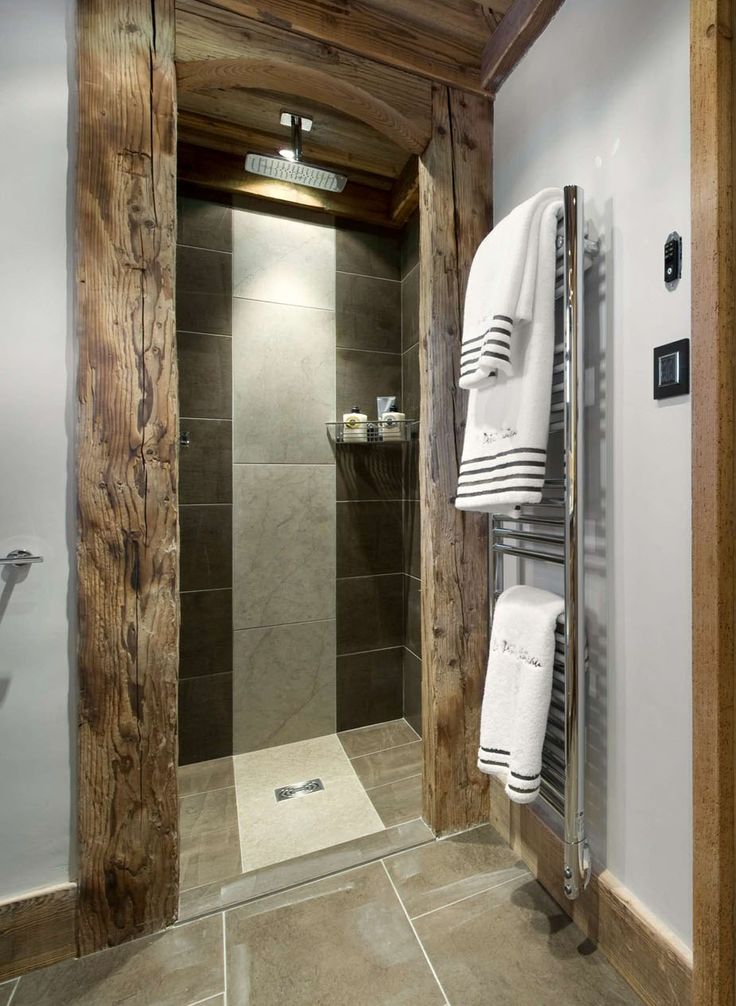 A modern chalet bathroom clad with tiles, with concrete and light stained rough wood framing the shower space