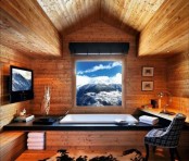 a stylish and cool chalet bathroom clad with light-stained wood, with a view, a TV, a chair, towels, lamps and a blanket
