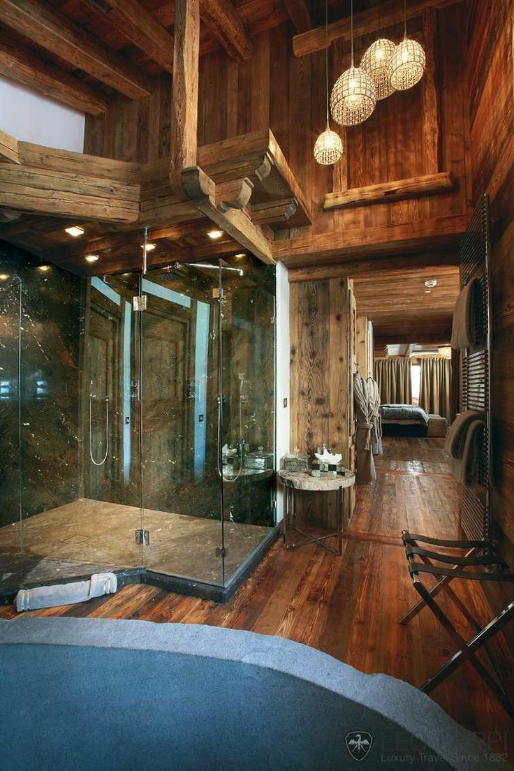 A large chalet bathroom clad with rich stained wood, with windows, a large glass enclosed shower and lamps