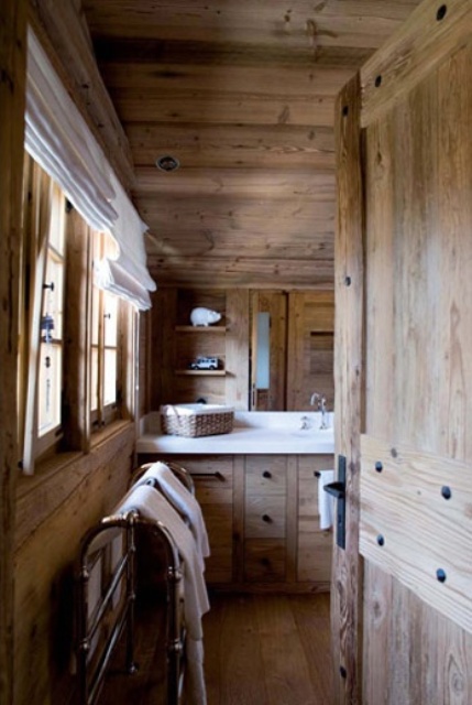 A light stained chalet bathroom clad with wood, with all wood everything, a large mirror, built in shelves and neutral textiles