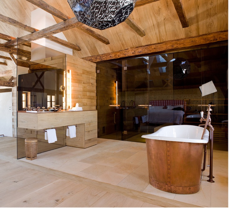 A contemporary chalet bathroom with light stained wood wall and a ceiling, a steam room with black glass, a tub clad with copper is amazing