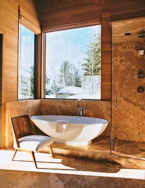 A chalet bathroom clad with light stained wood and stone, with windows for a view, an oval tub and a glass enclosed shower space
