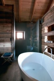a modern chalet bathroom fully clad with reclaimed wood, with some windows for natural light and an oval free-standing tub