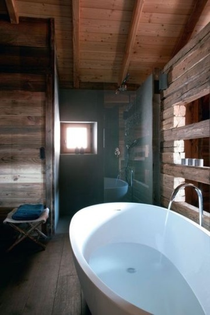 A modern chalet bathroom fully clad with reclaimed wood, with some windows for natural light and an oval free standing tub