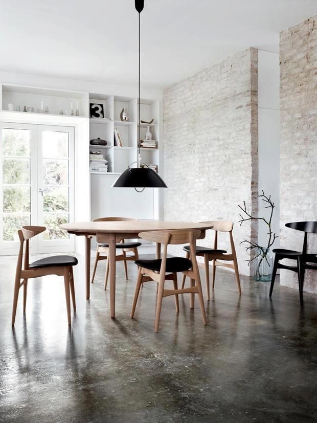 A Nordic dining room with whitewashed red brick walls, built in shelves and a chic modern dining set with a black pendant lamp over it