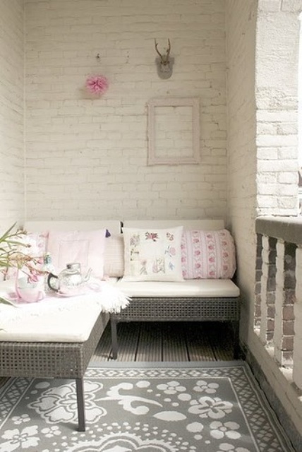 a balcony with whitewashed brick walls, a small sectional rattan sofa and printed pillows